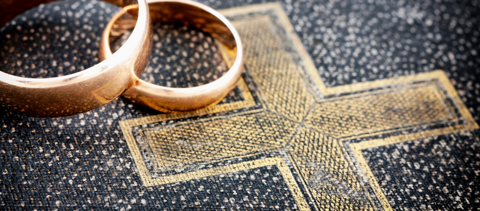 Two Gold wedding rings resting on a Black Bible Cover with a gold embossed cross